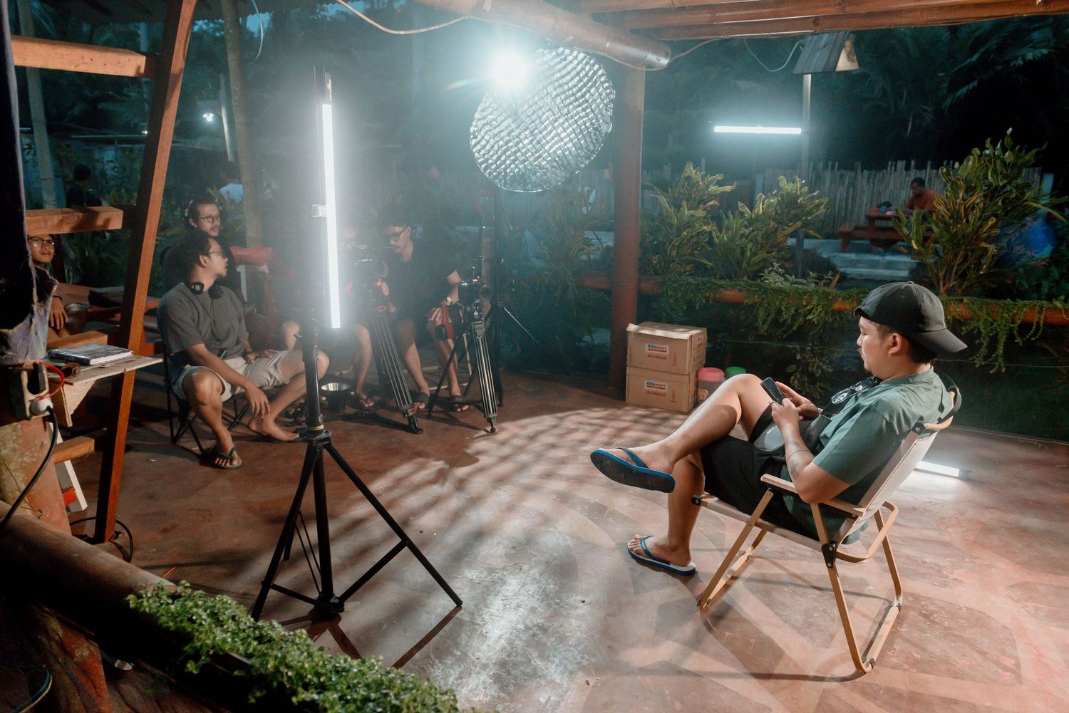 Behind the scenes photoshoot setup with lighting equipment and camera gear in outdoor nighttime setting.