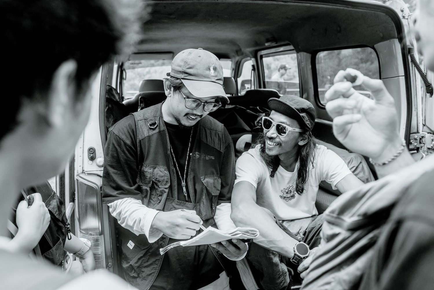 A black and white photograph of people sitting in a car looking at papers together.