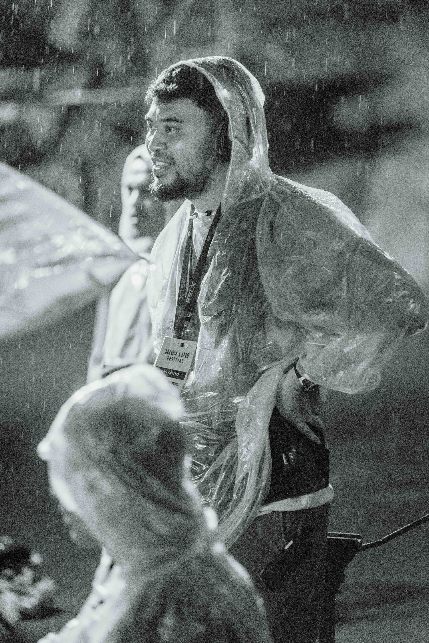 People wearing clear plastic rain ponchos stand in heavy rainfall during an outdoor event.