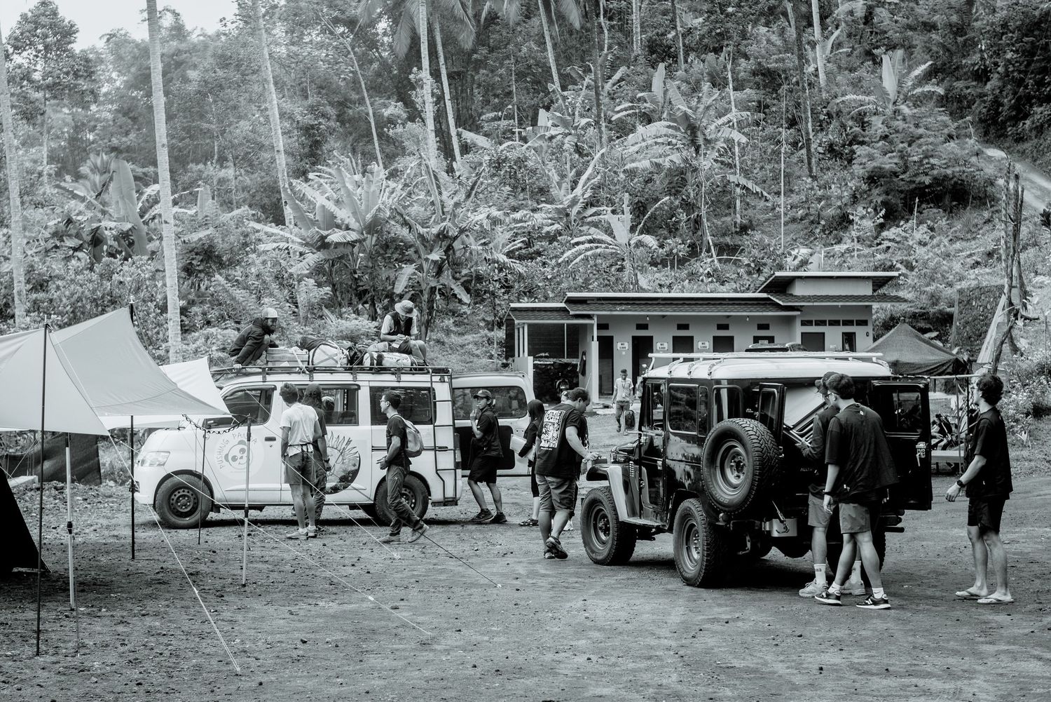 Vintage black and white photo showing campers and vehicles at a campsite with tents and trailers in a wooded area.