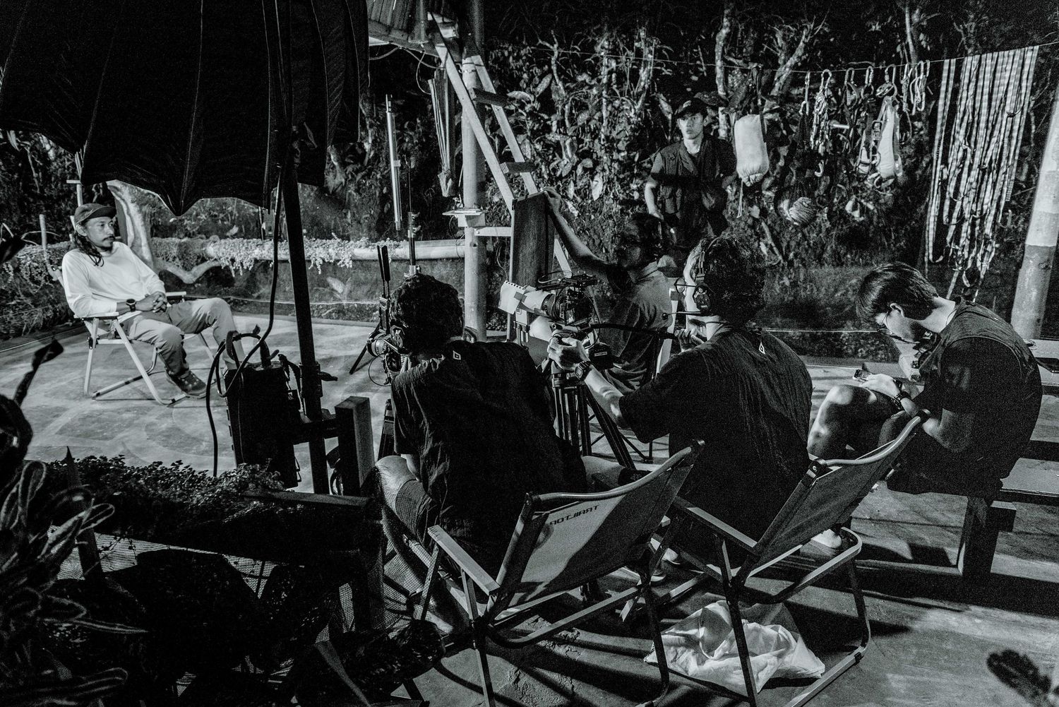 Black and white photo of people sitting in chairs around a film set during a night production shoot.