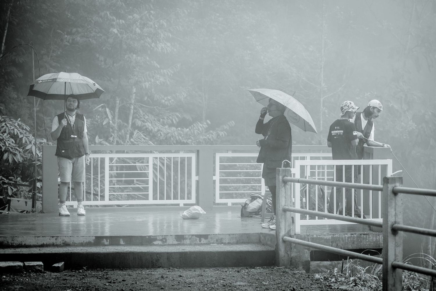 A series of black and white photographs showing people with umbrellas walking in the rain along a railing.