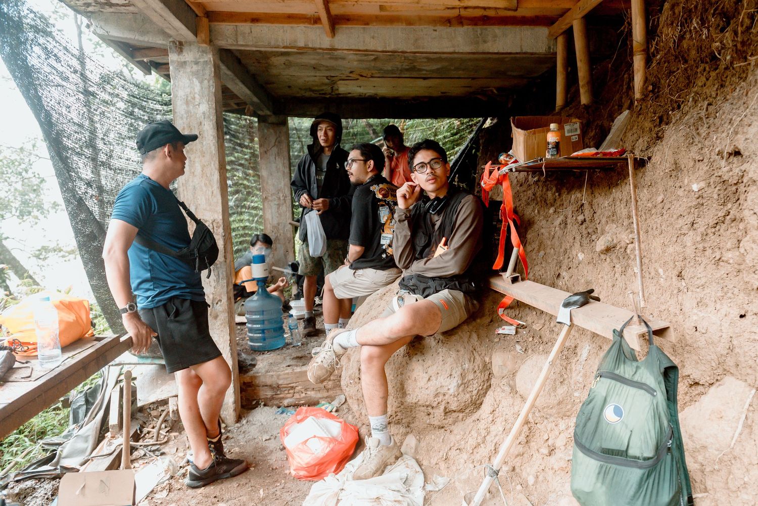 Hikers taking a break at a rustic shelter on a mountain trail with backpacks and gear scattered around.