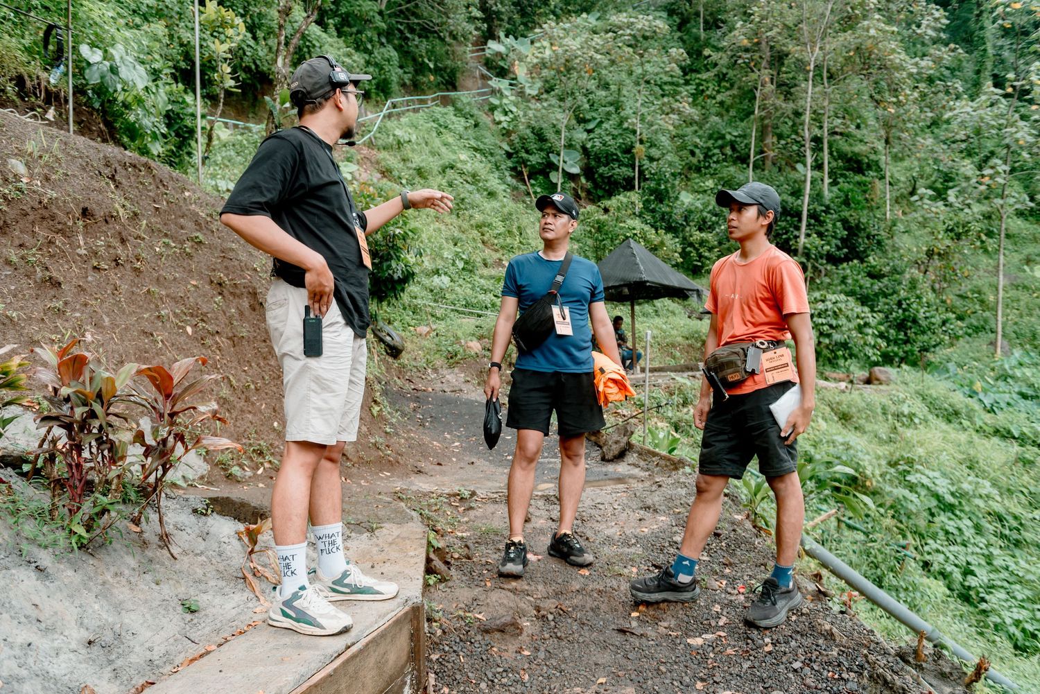 Hikers navigate a narrow dirt trail winding through lush green forest terrain.