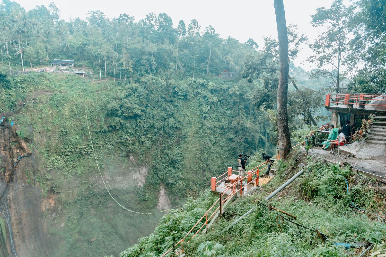 Panoramic view of a lush green mountainside with dense forest and winding paths in a tropical setting.