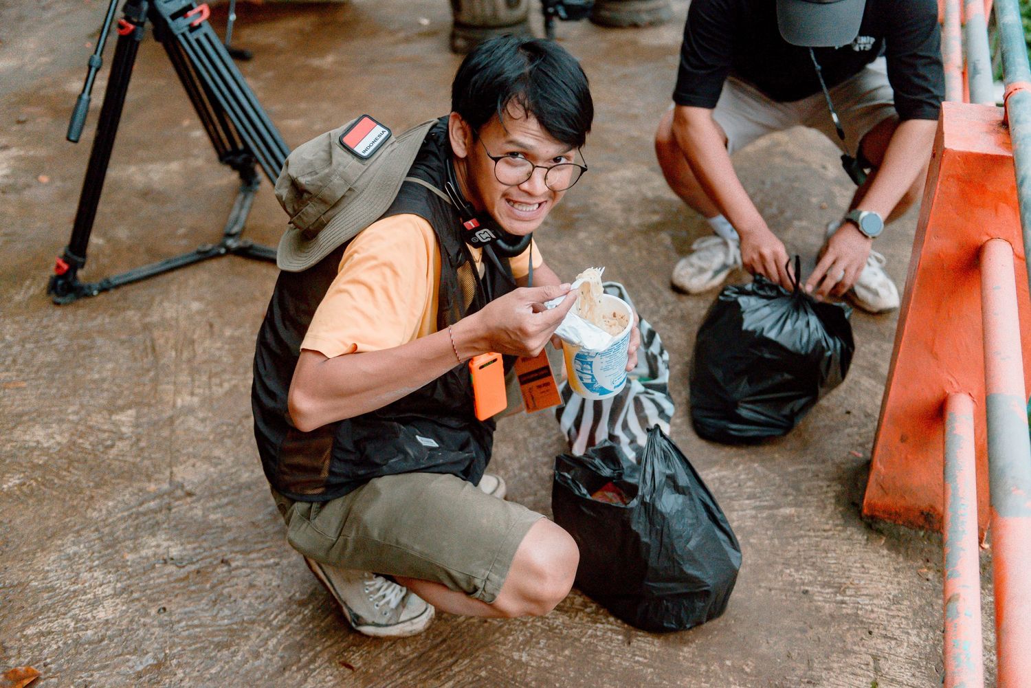 A climber in a black tank top takes a break to hydrate while sitting on the ground with climbing gear nearby.