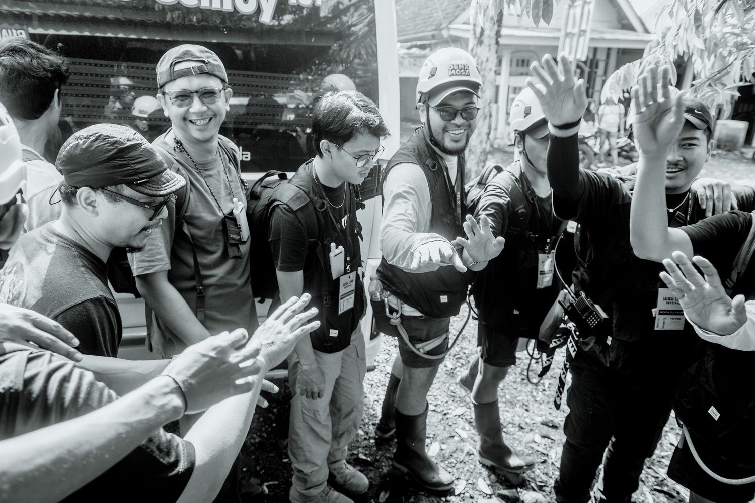 A black and white photograph shows a group of people clapping and celebrating together on a street.
