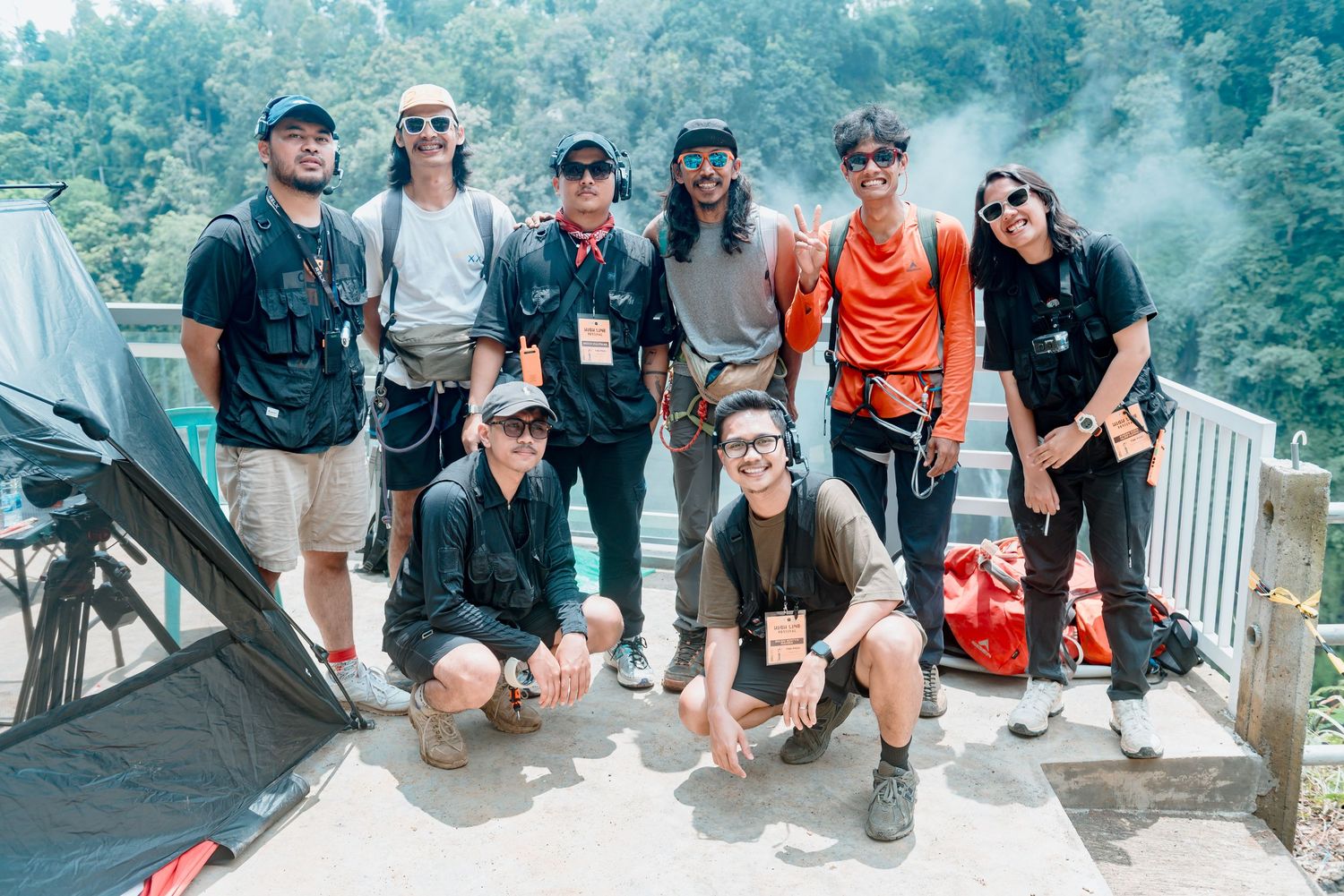 A group of hikers with backpacks and outdoor gear pose together on a misty mountain overlook.