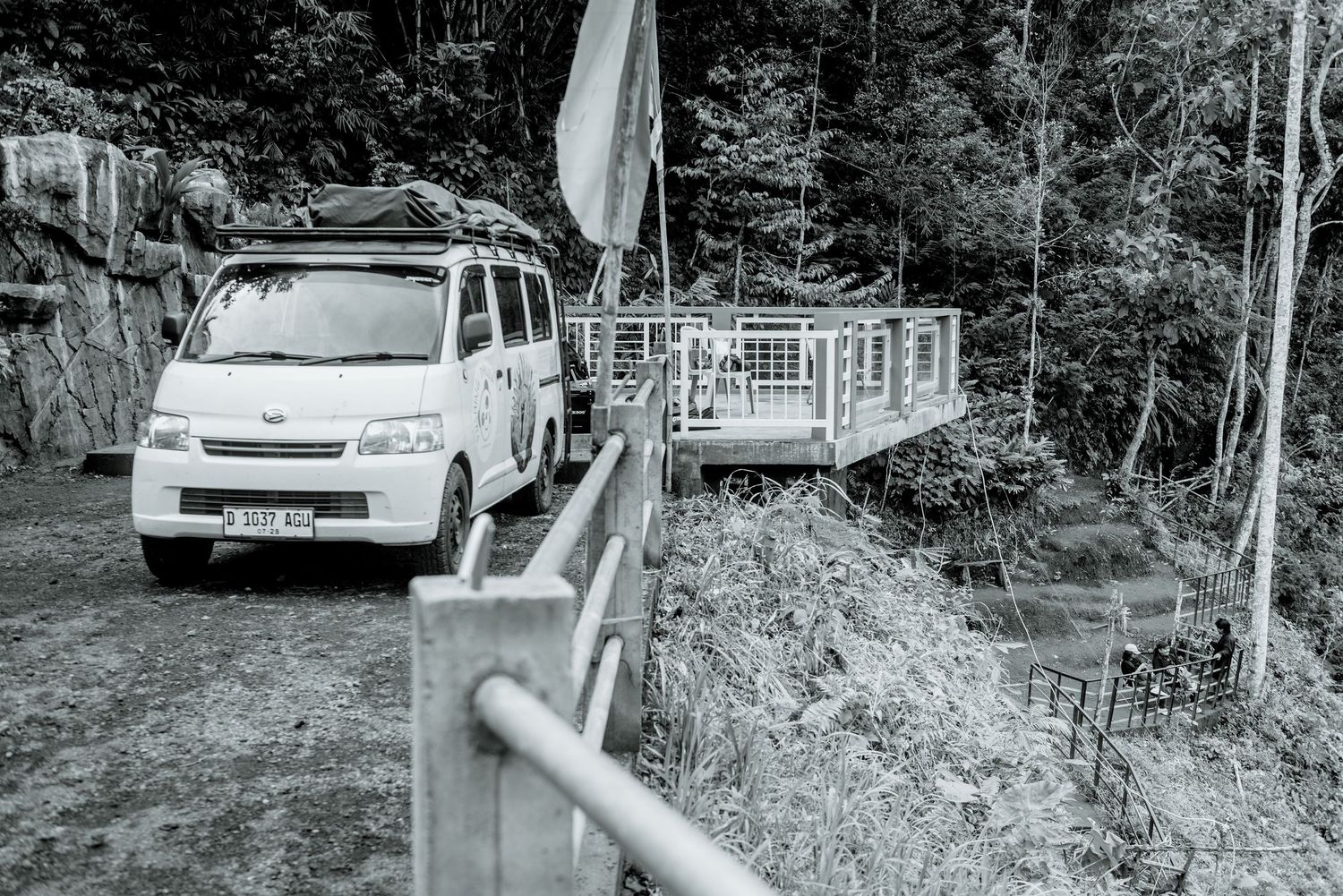 A long metal guardrail stretches along a winding mountain road with dense forest in the background.