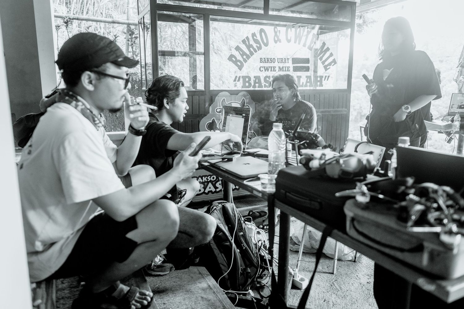 A black and white photograph of a radio station broadcast setup with turntables and microphones in a casual setting.