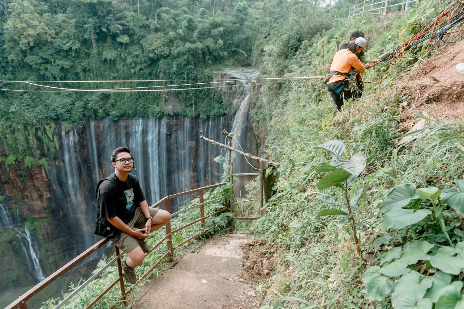 Two adventurers navigate a zip line course above a scenic waterfall surrounded by lush green vegetation.