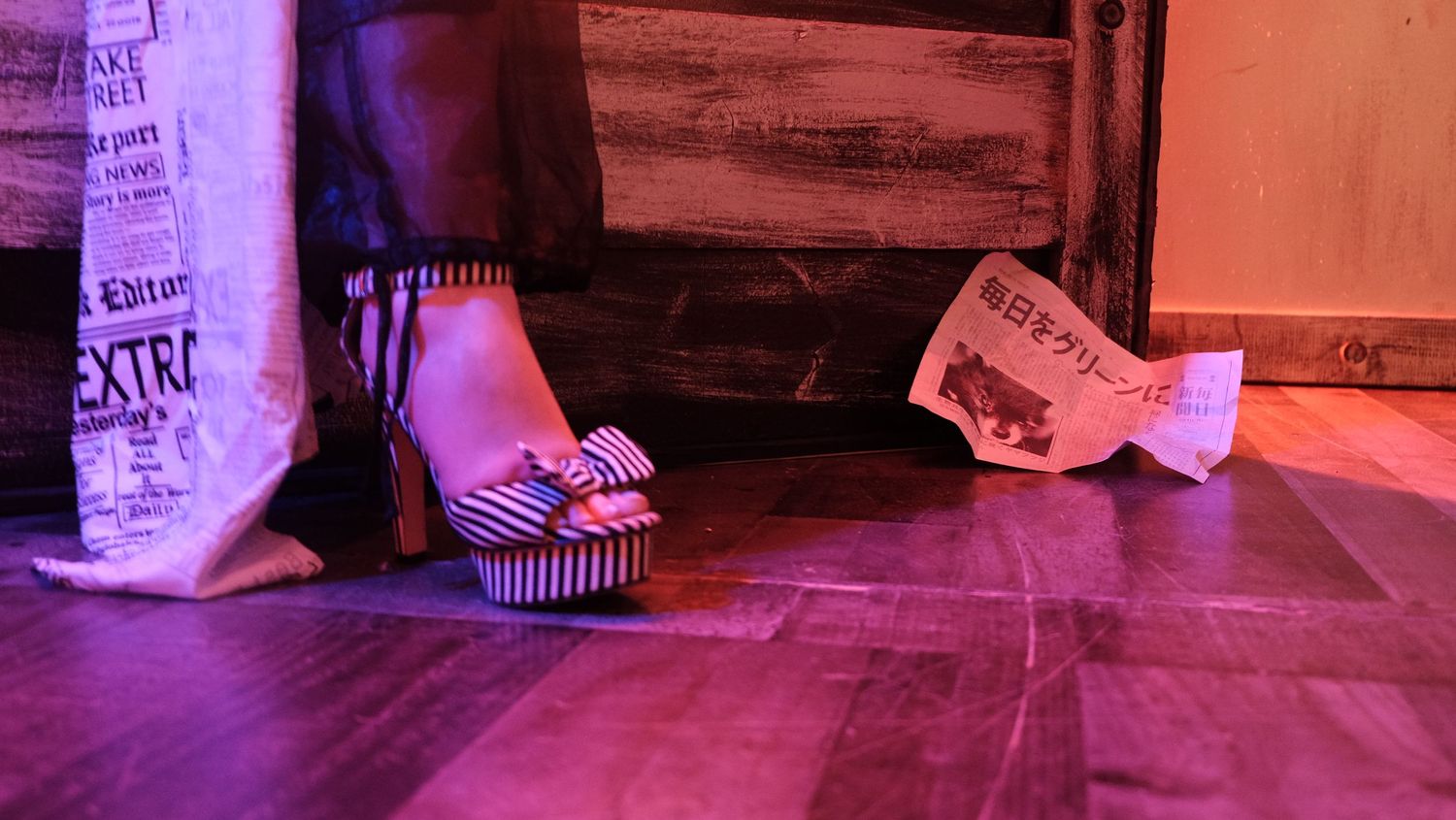 Colorful purple and orange lighting illuminates a dark wooden floor and wall corner creating a moody atmosphere.