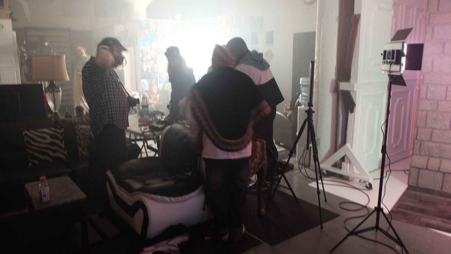 Behind the scenes view of a professional photo studio setup with lighting equipment and people working in a pink-lit space.