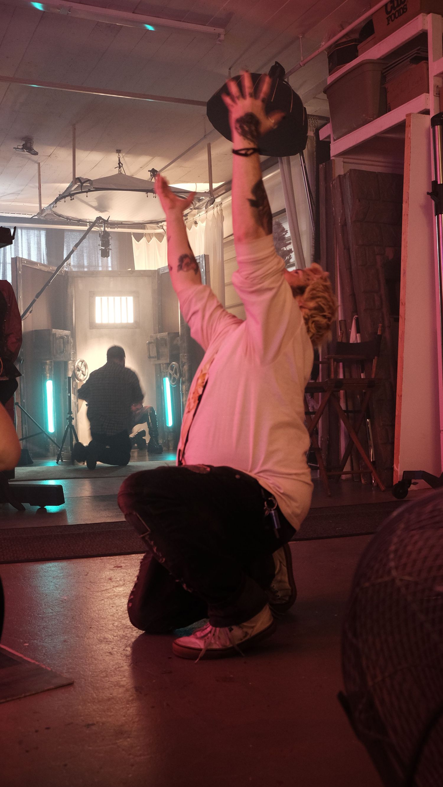 A person in a pink hoodie performs on a dimly lit stage with atmospheric blue lighting and fog effects.