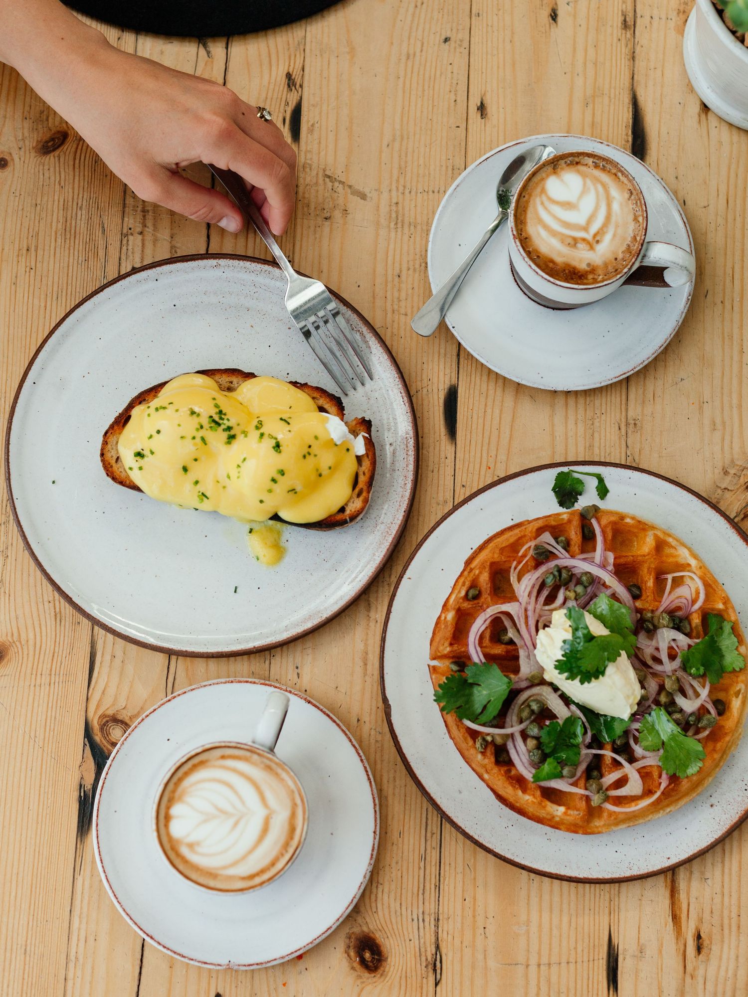 Breakfast spread on wooden table with eggs, coffee, and various dishes.