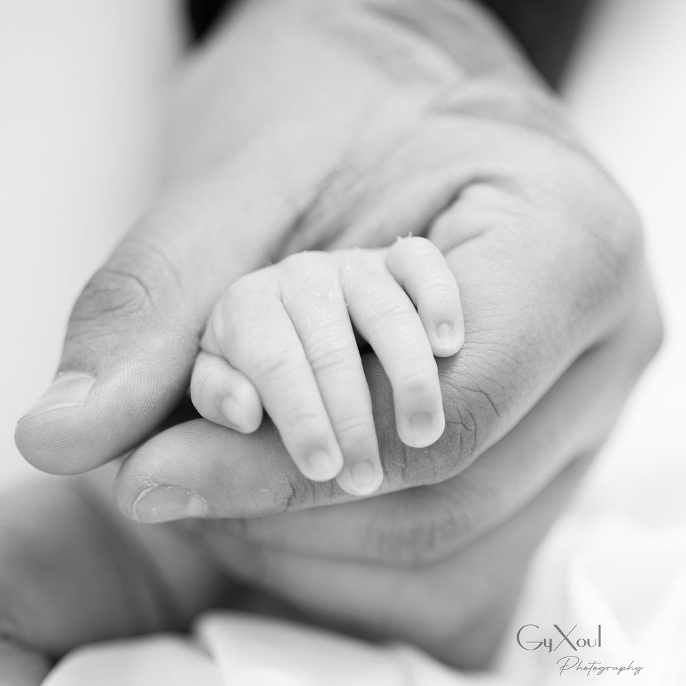 Monochrome image of tender hands cradling a newborn's tiny foot.