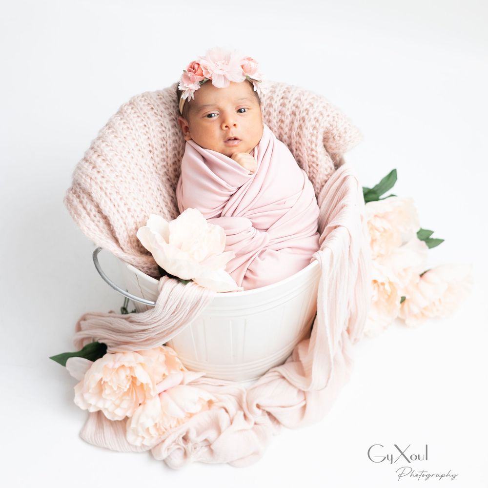 Newborn baby wrapped in soft pink swaddle blanket with peach roses in white basket.