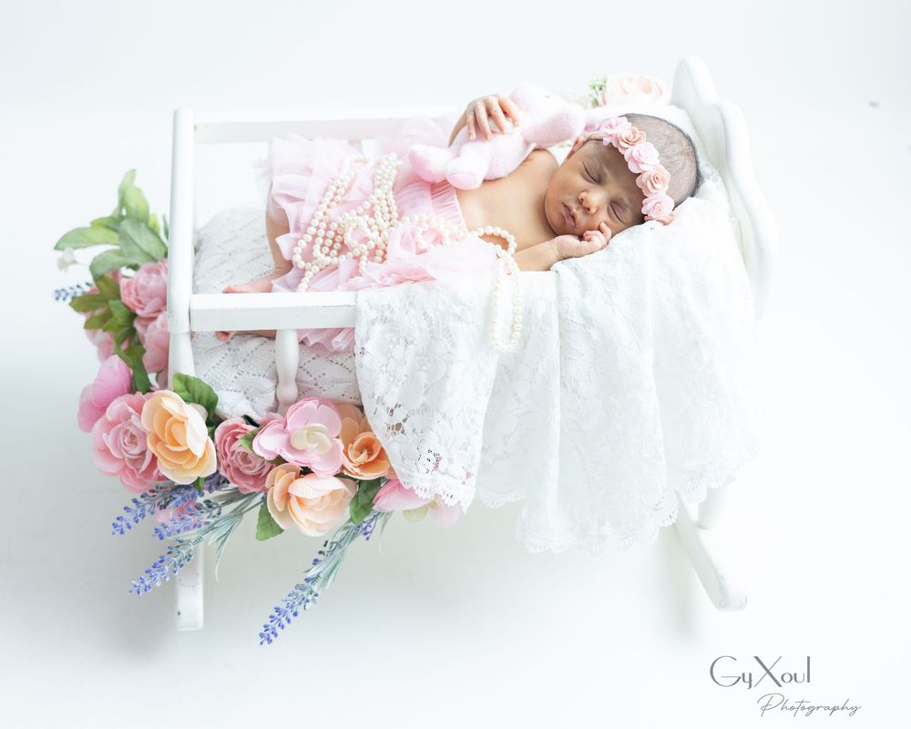 Delicate newborn portrait series with white lace and pink flower arrangements.