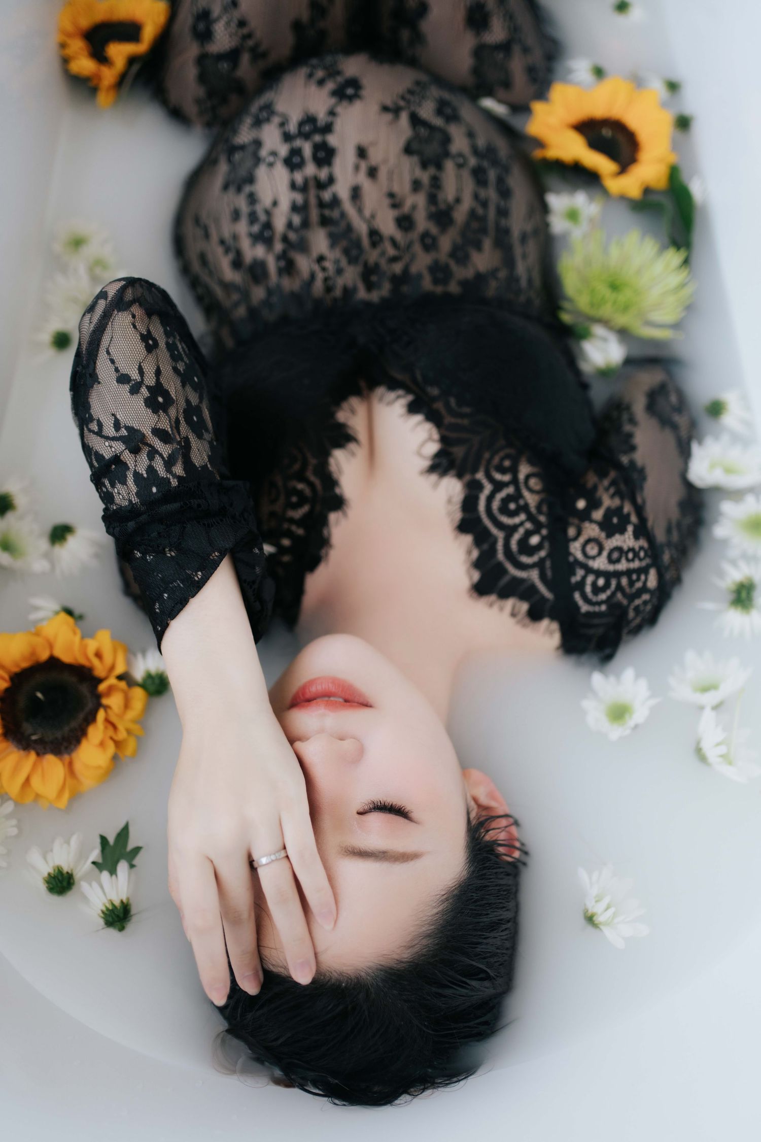 Artistic portrait in milk bath with black lace dress and sunflowers, creating ethereal dreamy atmosphere.身穿黑色蕾絲連身裙，沐浴在牛奶中，周圍環繞著向日葵的藝術肖像