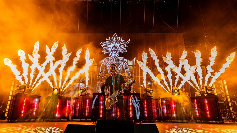 Spectacular fireworks and pyrotechnics display illuminates a stage with bright orange flames and white sparklers at night.