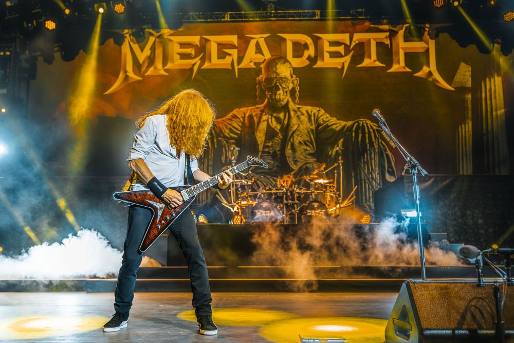 Heavy metal band Megadeth performs on stage with dramatic lighting and smoke effects during a live concert.