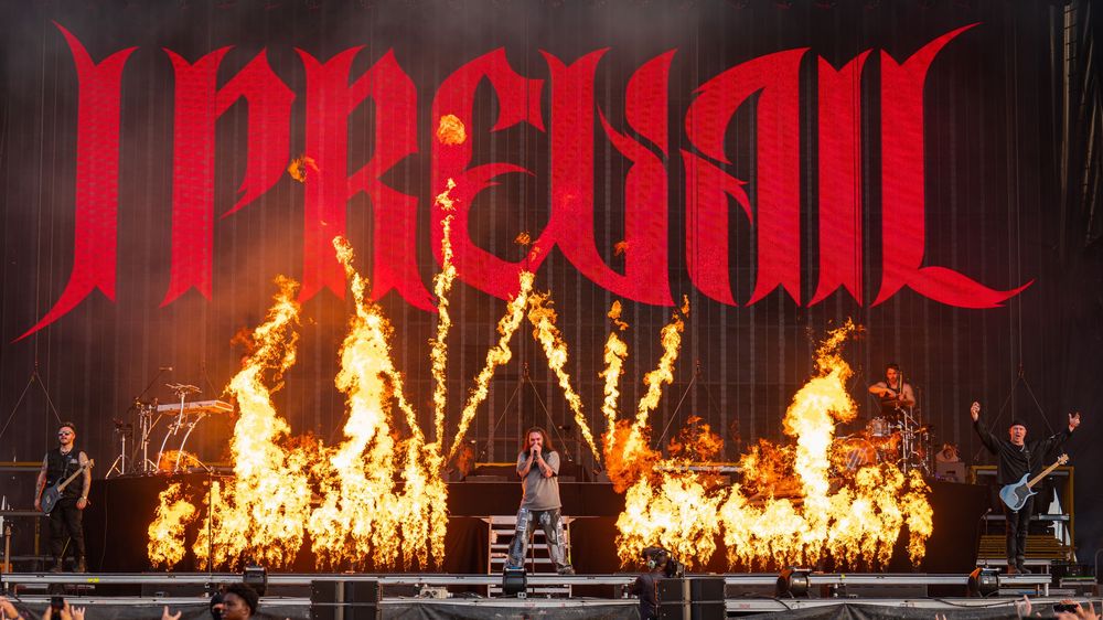 A dramatic concert stage performance with bright flames and pyrotechnics creating an intense atmosphere during a live show.