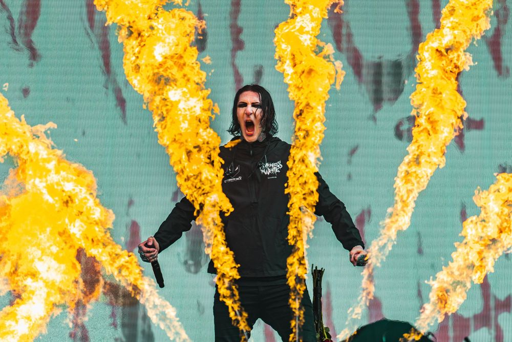 Multiple flame jets shoot upward during a stadium event with green seats visible in the background.