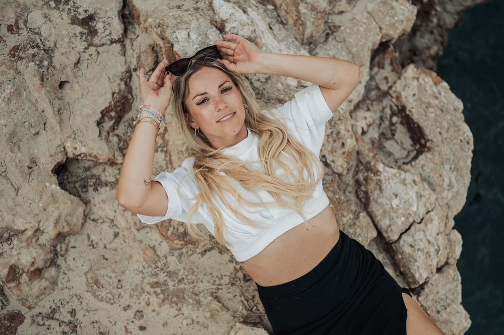 Lifestyle photoshoot featuring a person in a white top posing against rugged coastal rocks at sunset.