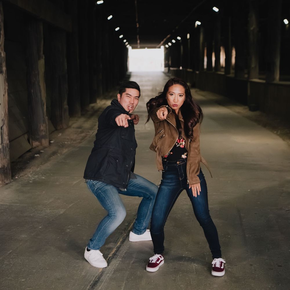 Fun couple posing and pointing at camera in dark urban tunnel corridor with dramatic lighting.