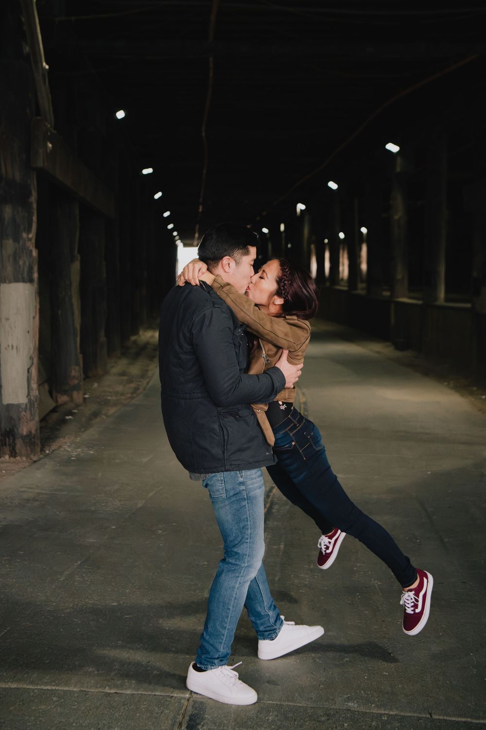 Man lifting woman for a kiss in a dimly lit urban tunnel during nighttime engagement session.