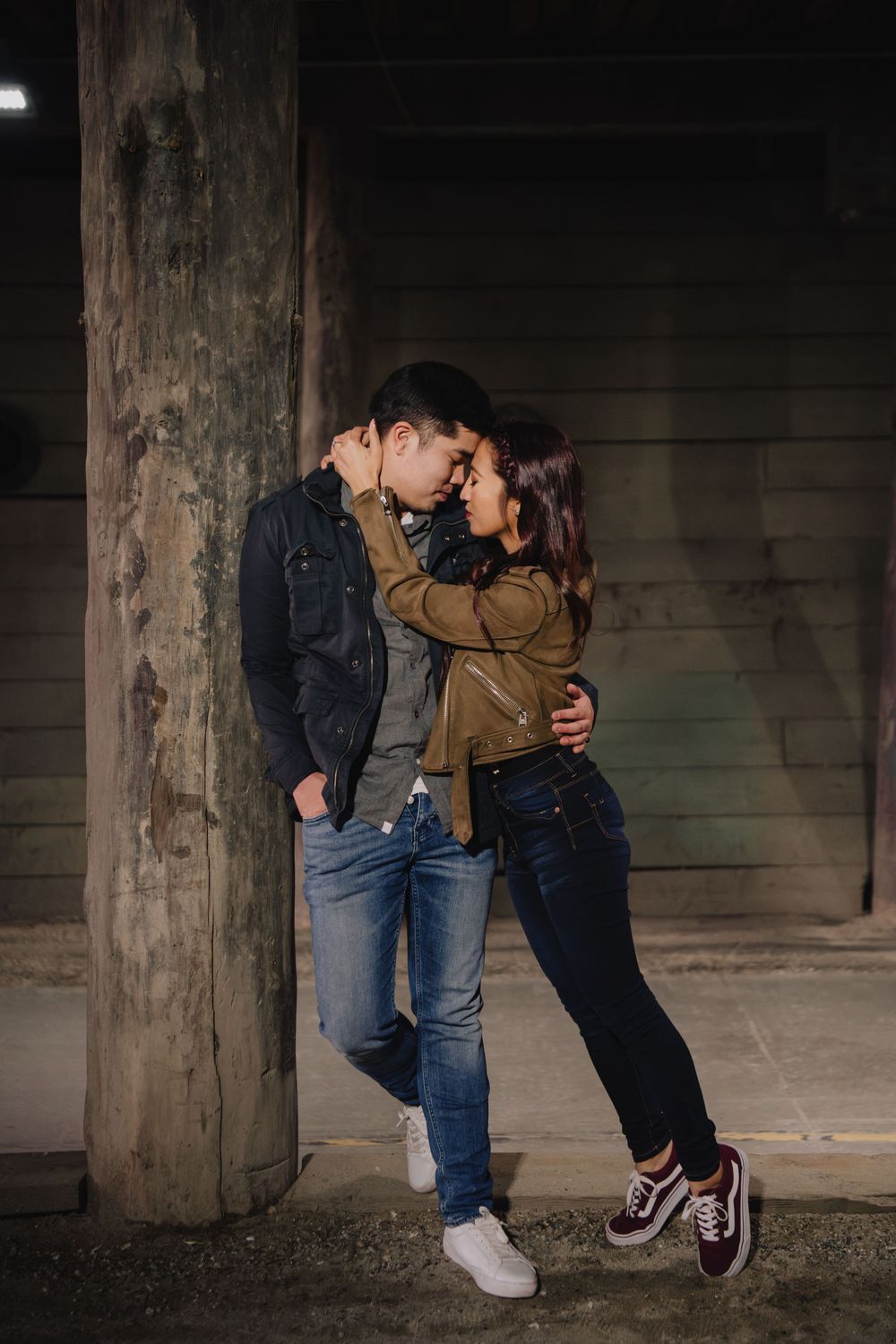 Couple leaning against wooden pillar sharing an intimate moment in a dark urban tunnel setting.