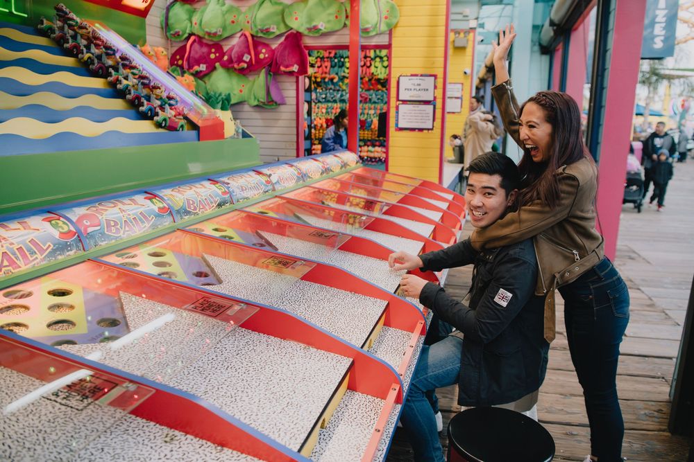 Young couple playing a carnival water game at a colorful boardwalk arcade.