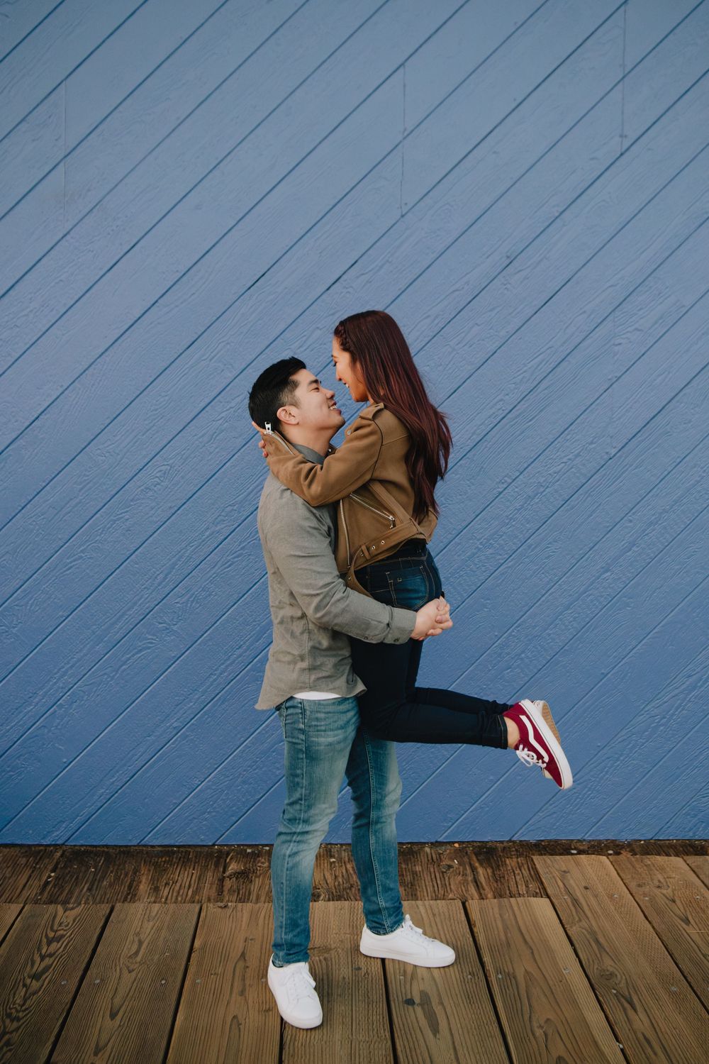 Romantic couple embracing against a vibrant blue wooden wall on a boardwalk.