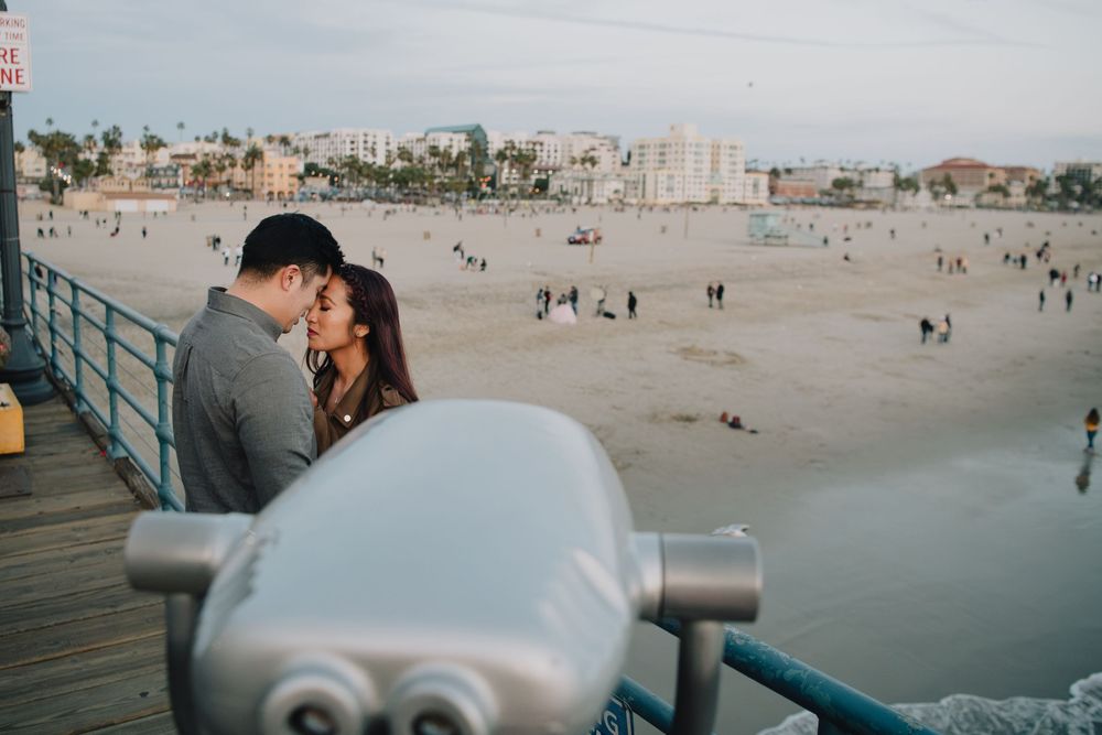Couple sharing a romantic moment on a pier overlooking a busy sandy beach.