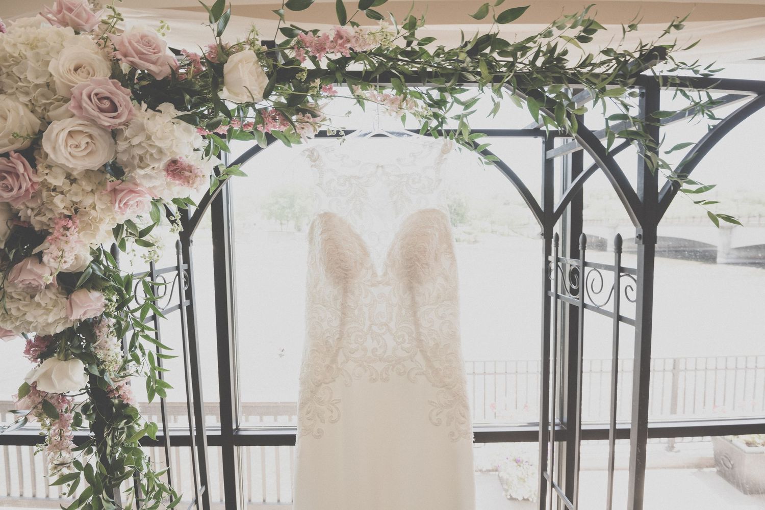 Wedding dress hanging from decorative arch with pink and white floral arrangements.