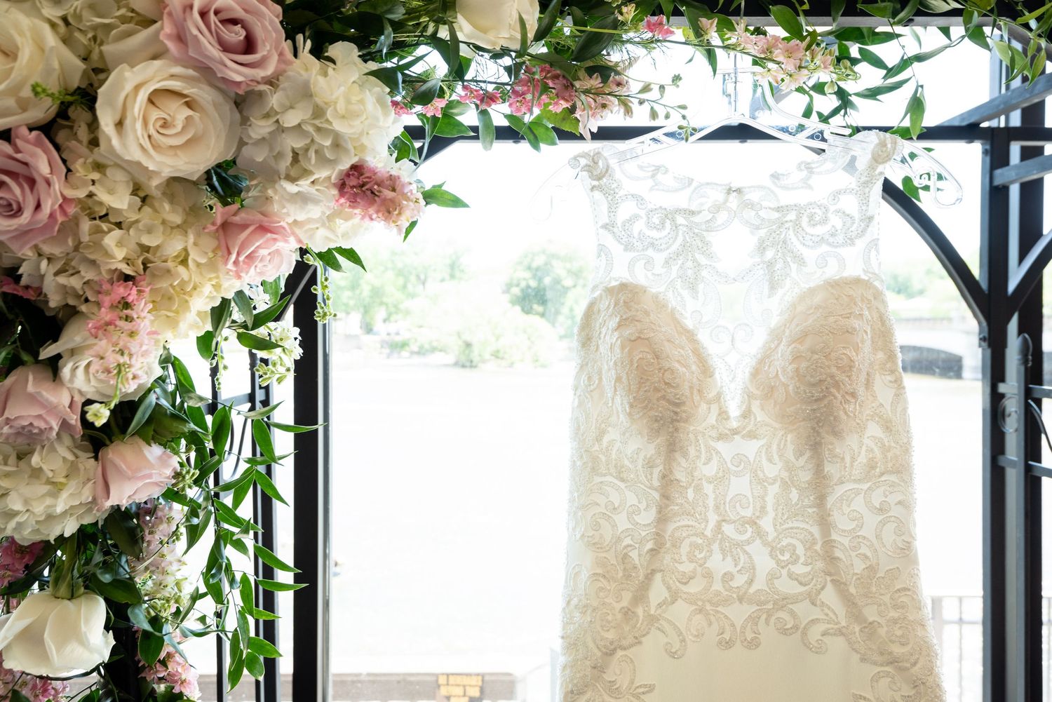 Elegant white lace wedding gown displayed on hanger with floral decorations.