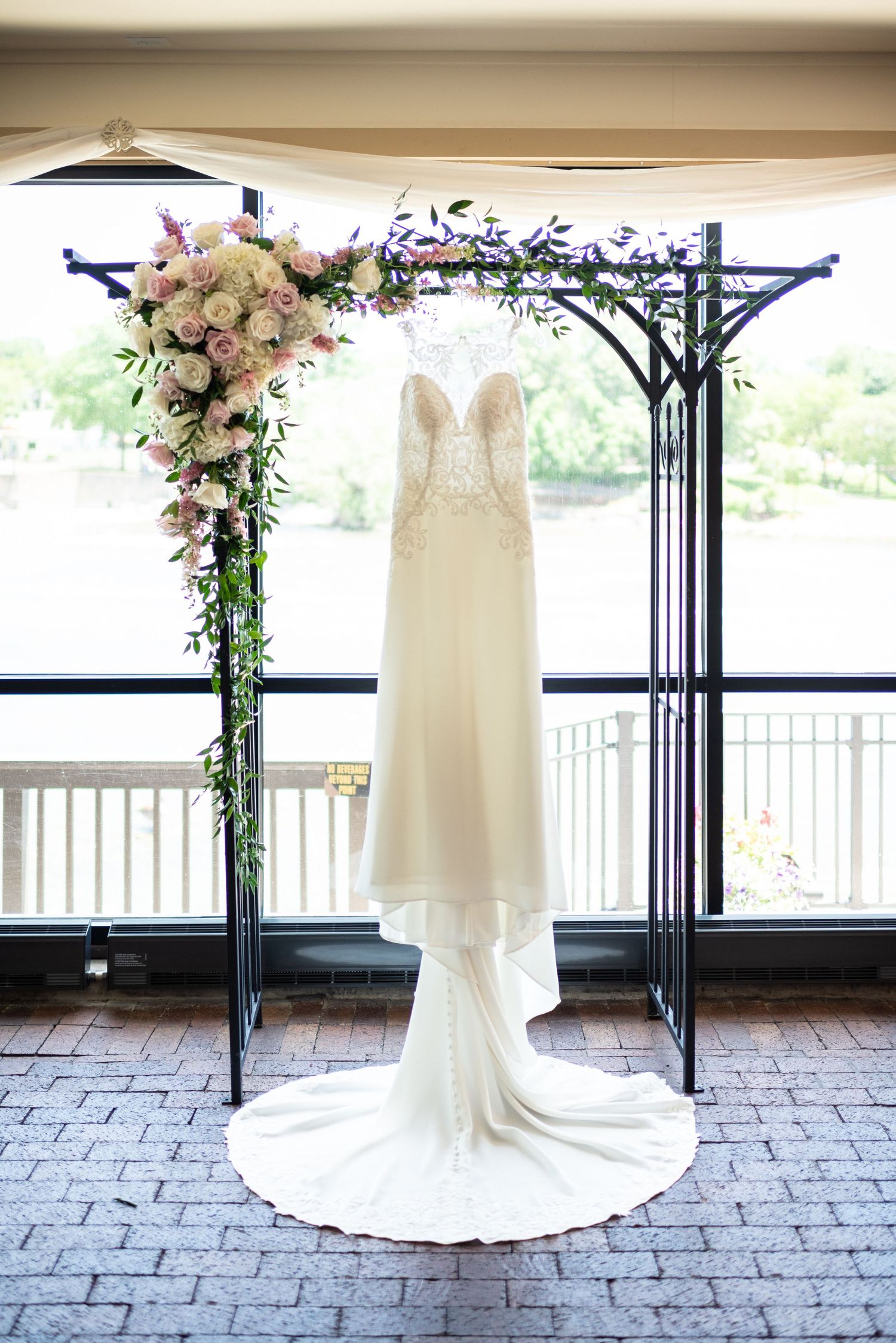 Full-length wedding dress displayed against stone patio with floral arch.