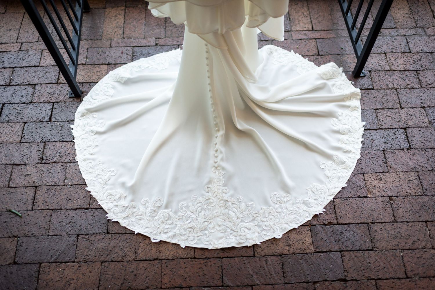 Close-up of wedding dress train spread out on brick patio.