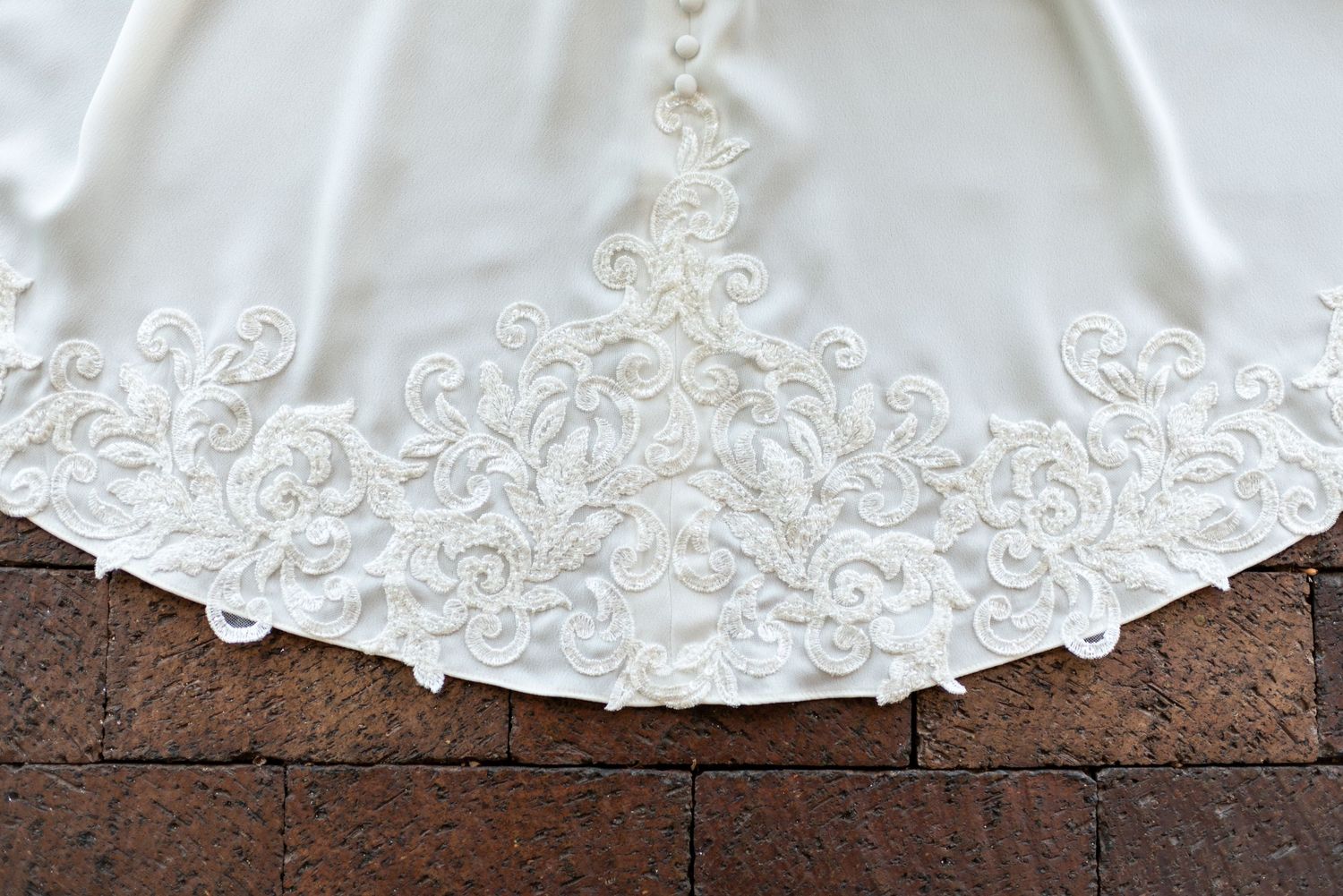 Detailed view of intricate lace embroidery on white wedding dress hem.