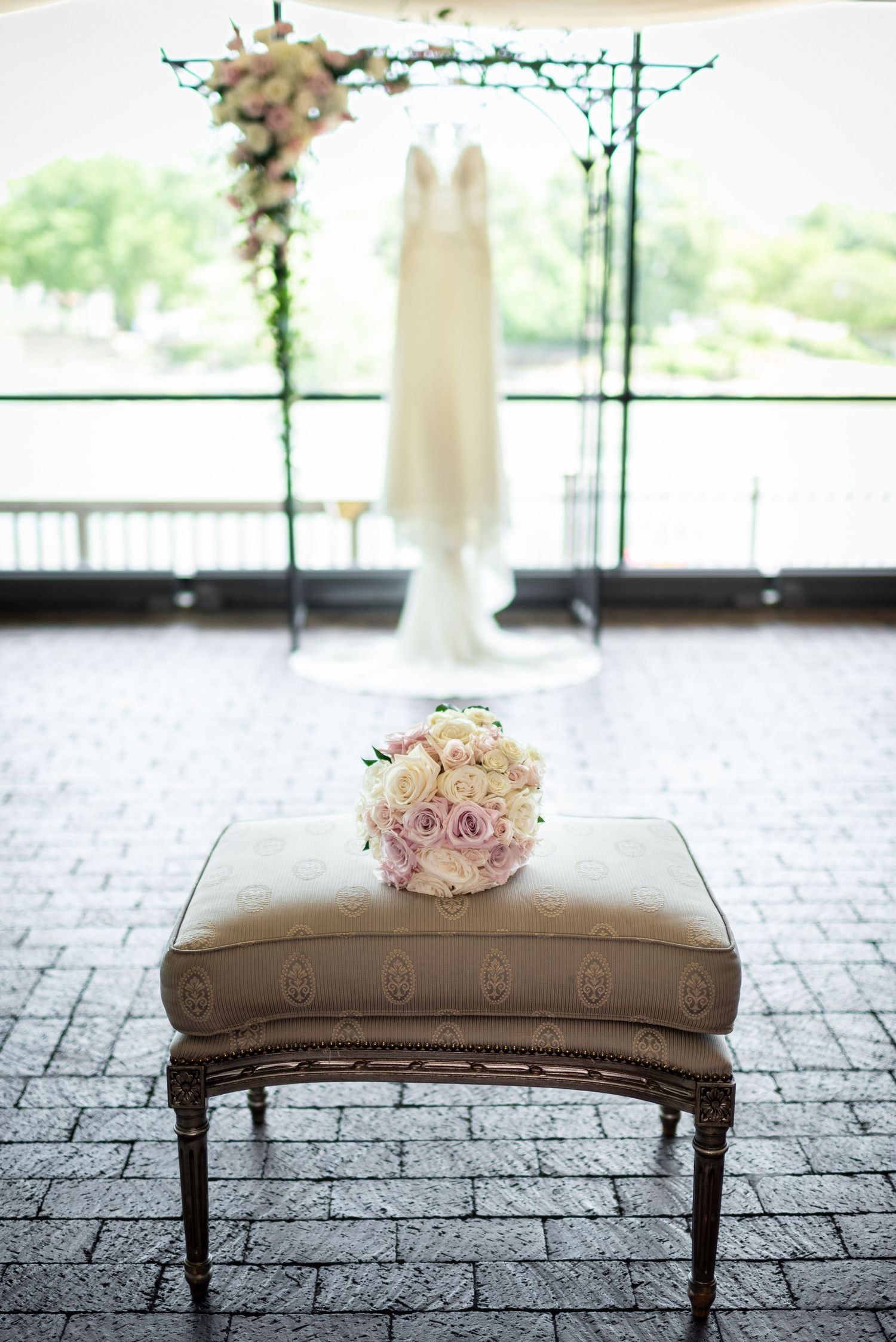 Pink and white bridal bouquet on vintage bench with wedding dress in background.
