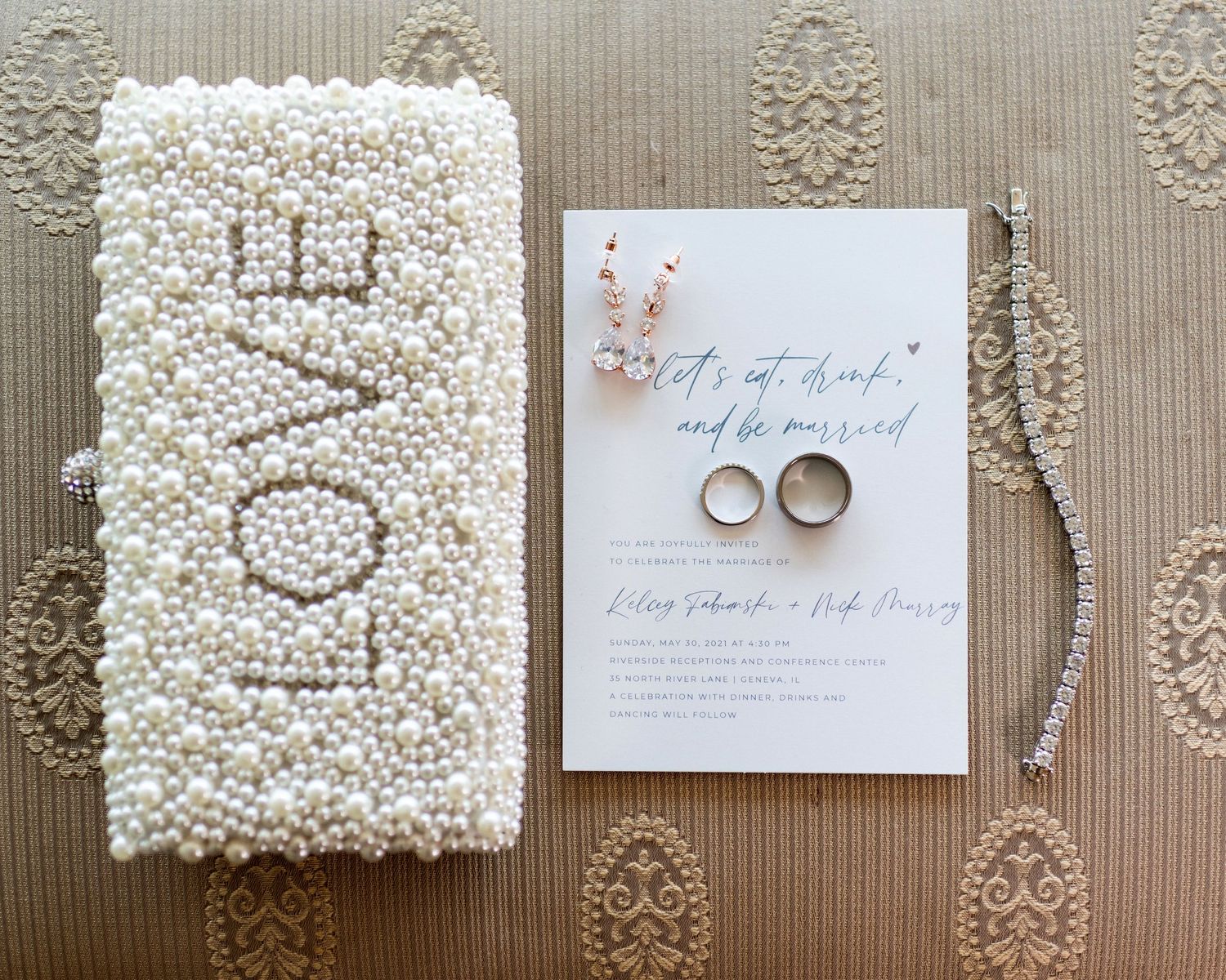 Wedding invitation suite with pearl details and wedding rings on textured background.