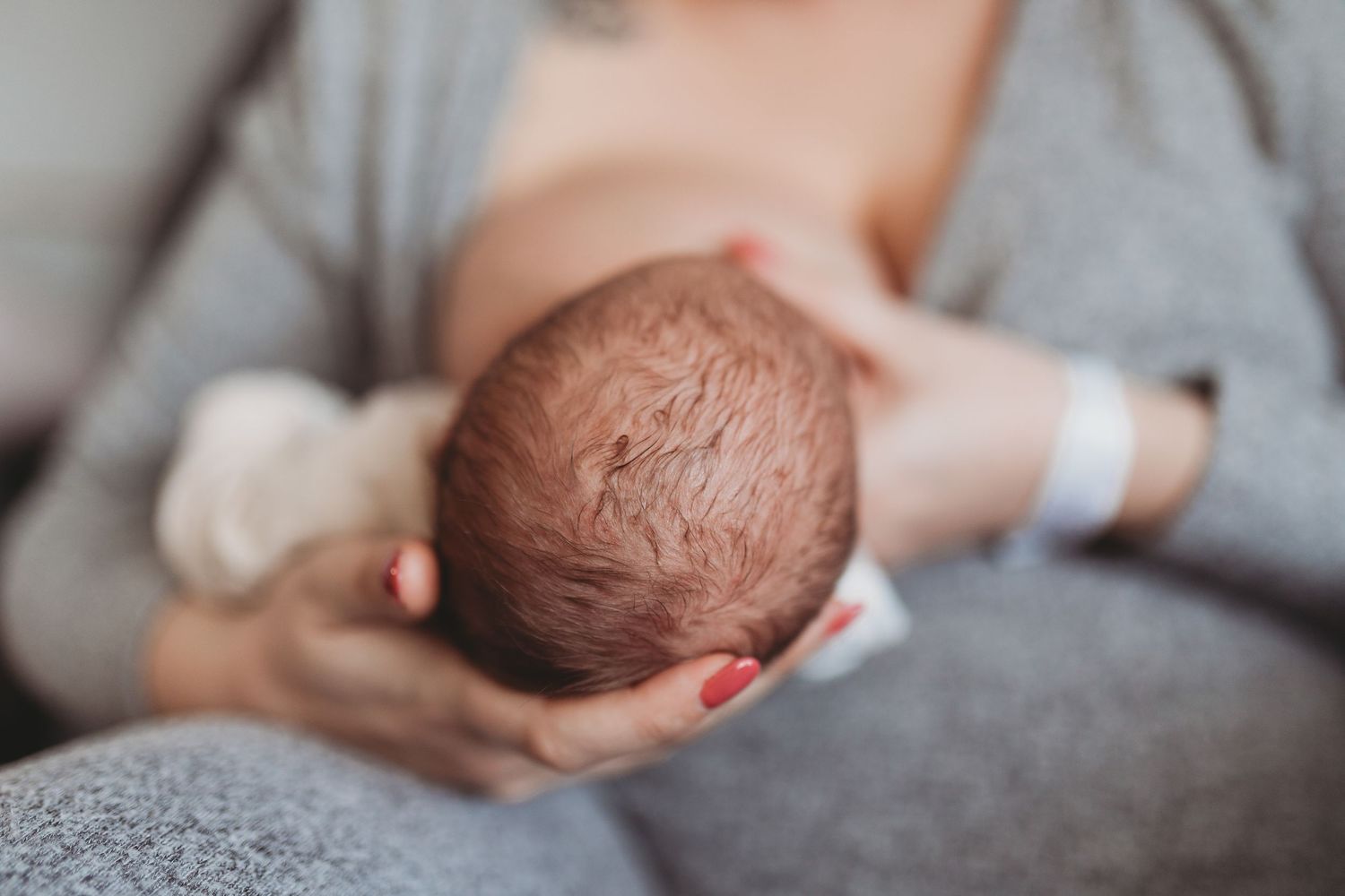 Newborn baby with brown hair sleeping peacefully on soft gray bedding in a series of gentle poses.