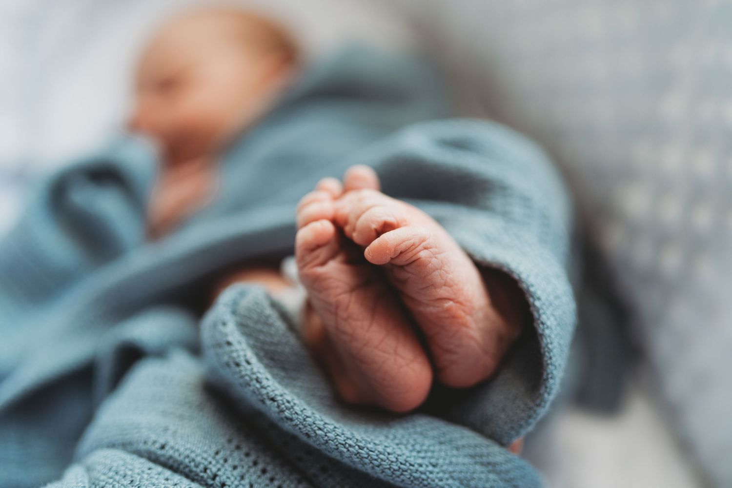 Close-up of a newborn baby's tiny fingers grasping a soft teal blanket in natural light.