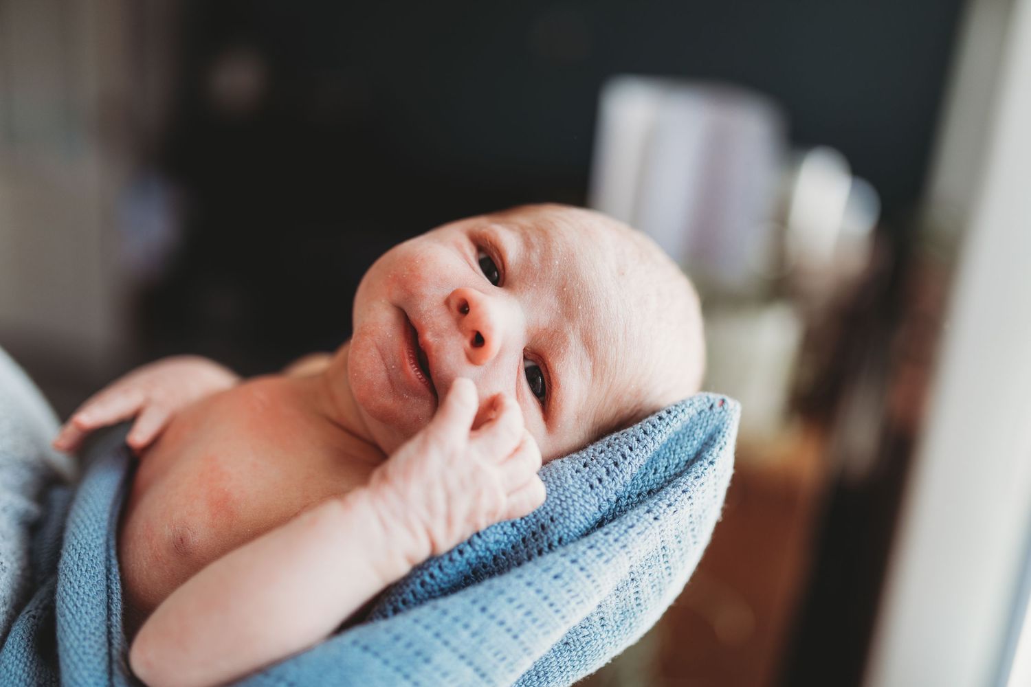 A newborn baby yawns while swaddled in a soft blue blanket.