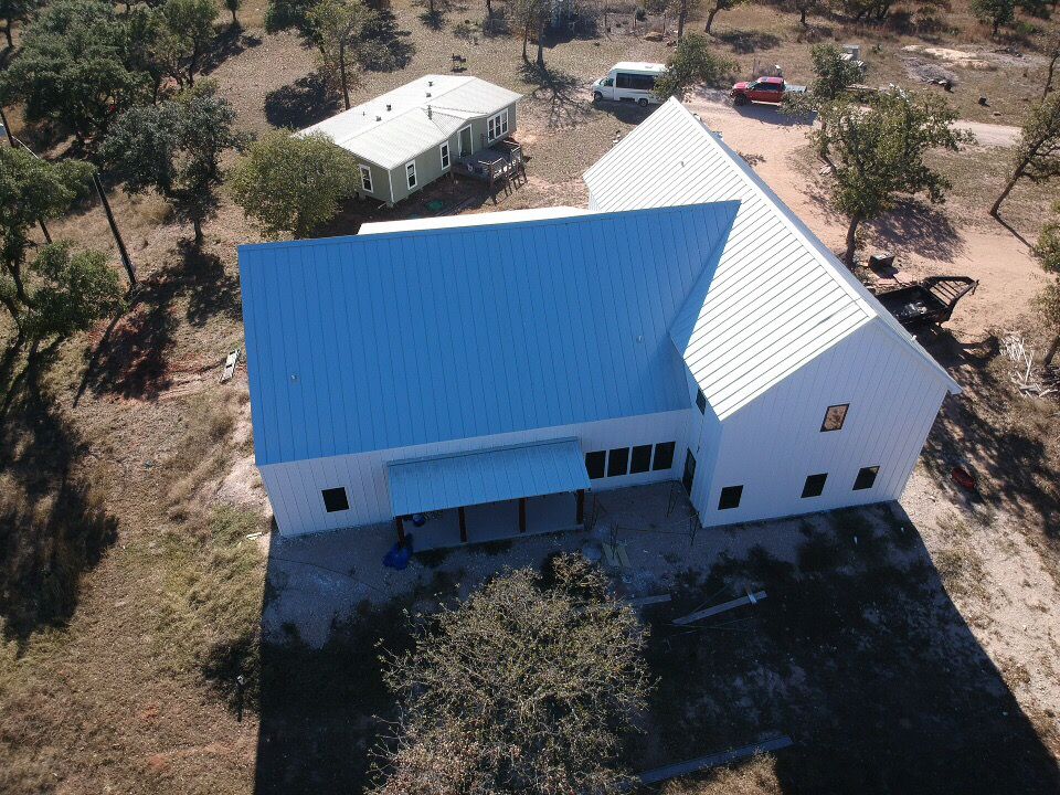Aerial view of white and blue metal buildings on a rural property.