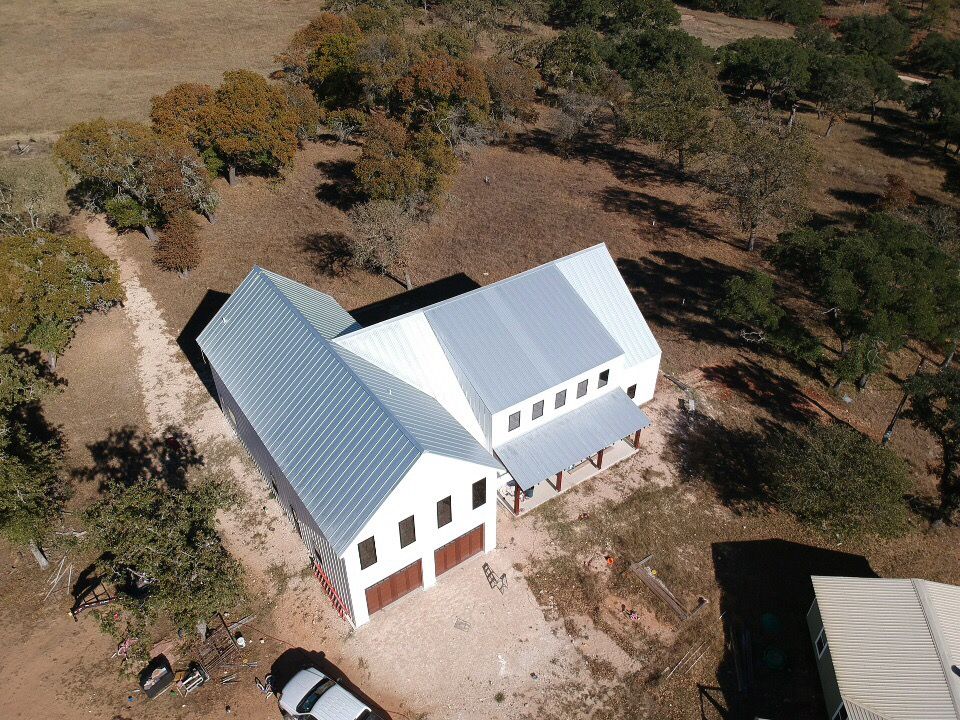 Drone shot of white buildings with metal roofing in a countryside setting.