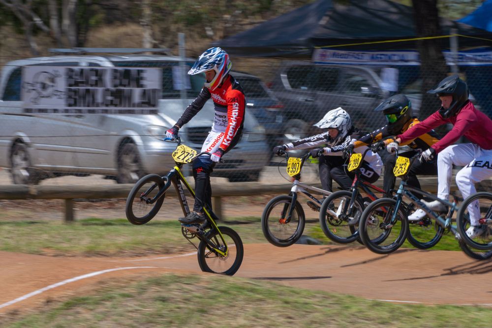 BMX riders racing and jumping on a dirt track during competition.
