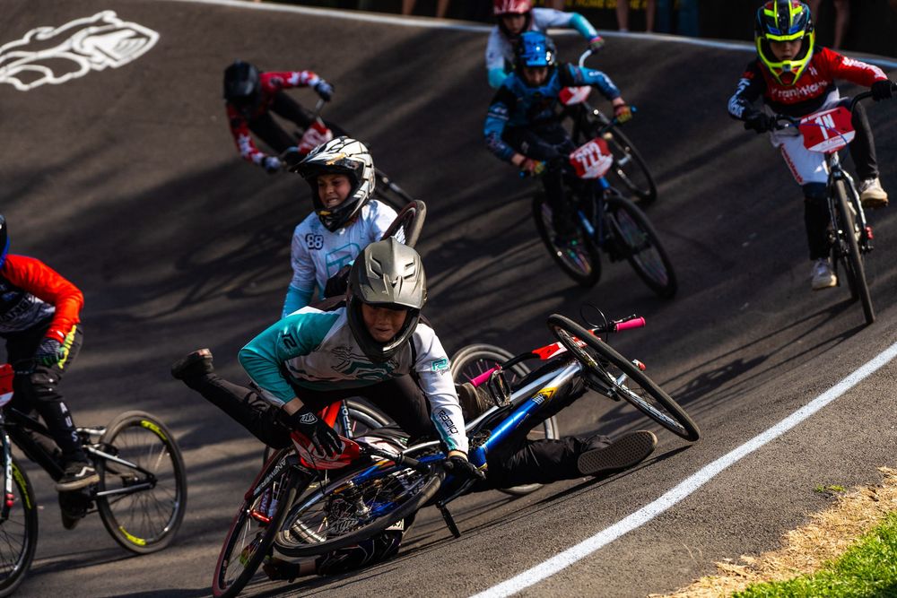 BMX racers compete on a track during a race, navigating a turn at high speed in colorful racing gear.