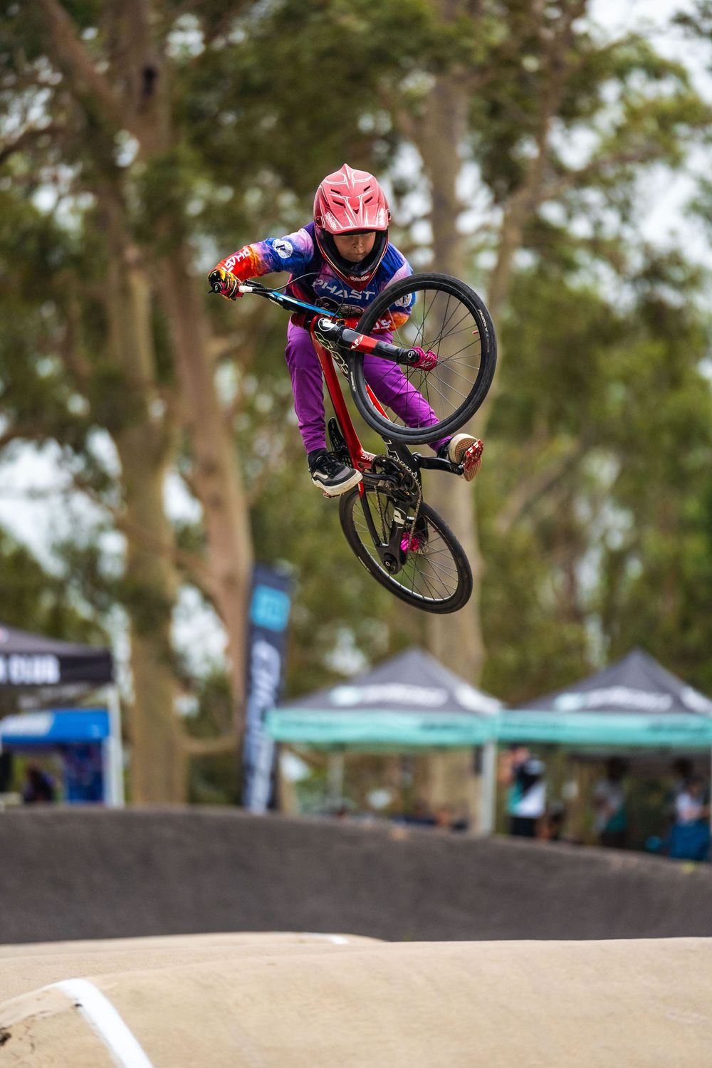 BMX rider performs impressive aerial tricks over dirt jumps during competition at outdoor bike park.