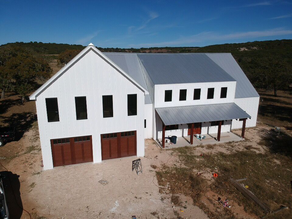 Modern stone house exterior with metal roof and large windows under construction.